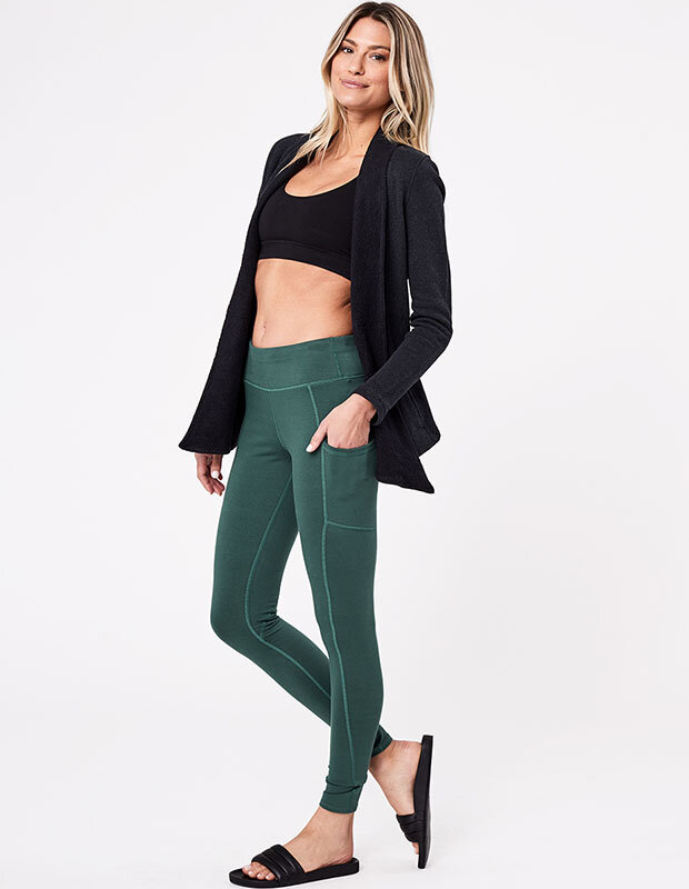 Woman in Pact organic green leggins with pocket, black sports bra and cardigan sweater
