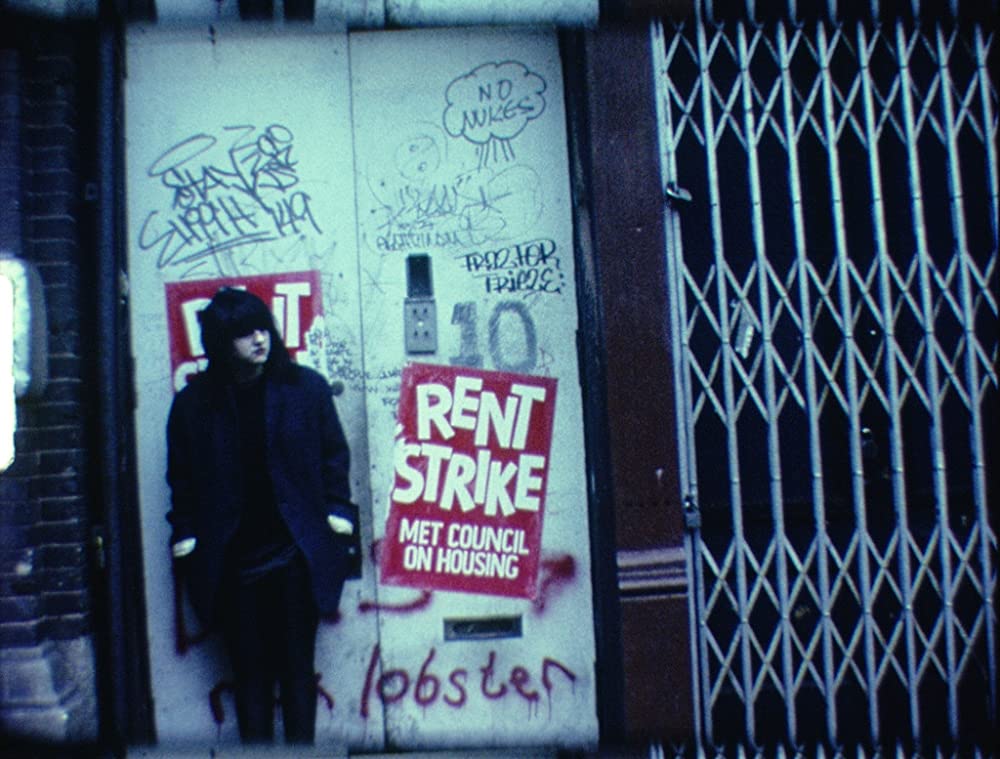 Film still Beauty becomes the Beast by Lydia Lunch - image of a woman on urban street with a rent strike poster behind her.