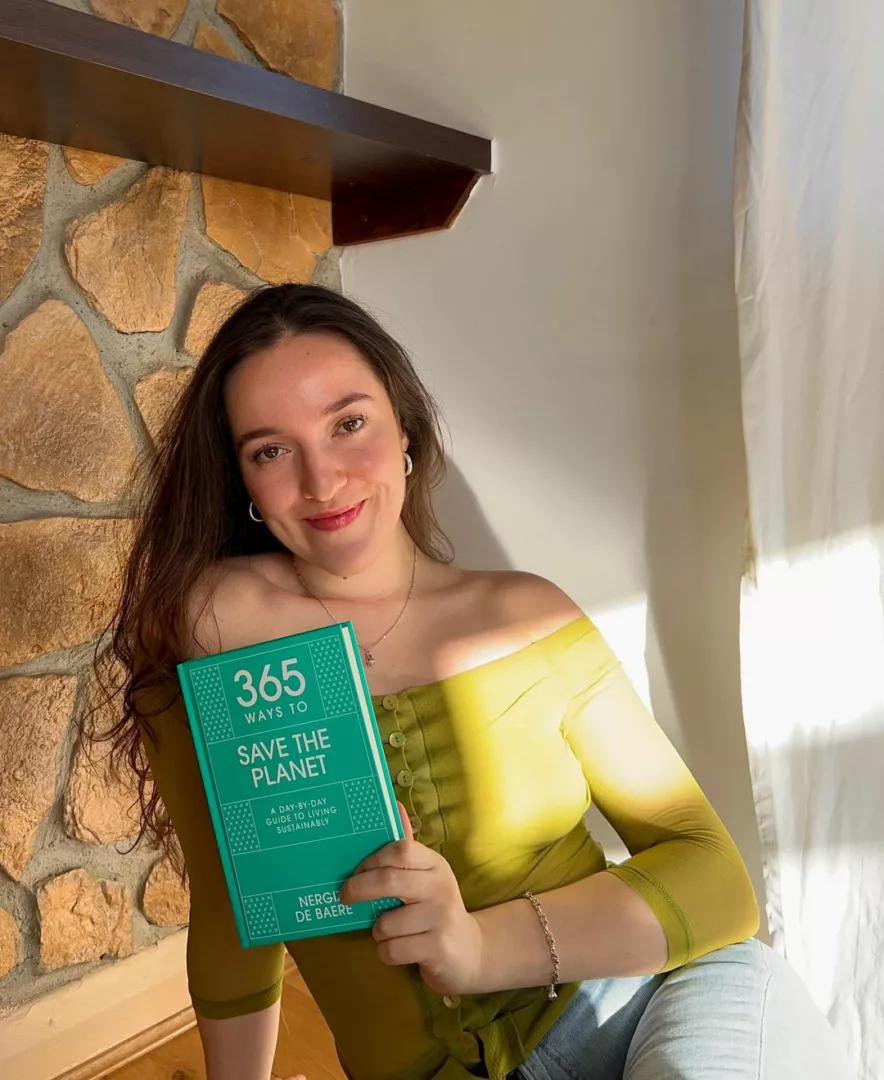 Negriz De Baere sitting and holding her book, 365 ways to save the planet.