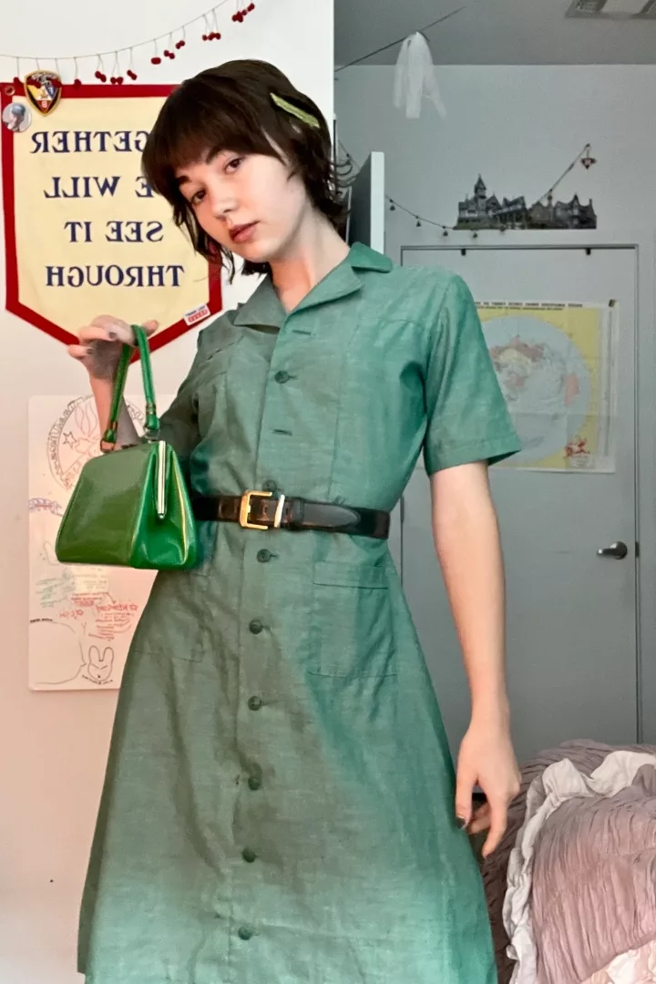 Harper Haynes wearing a girl scout uniform belted and with a green vinyl bag.