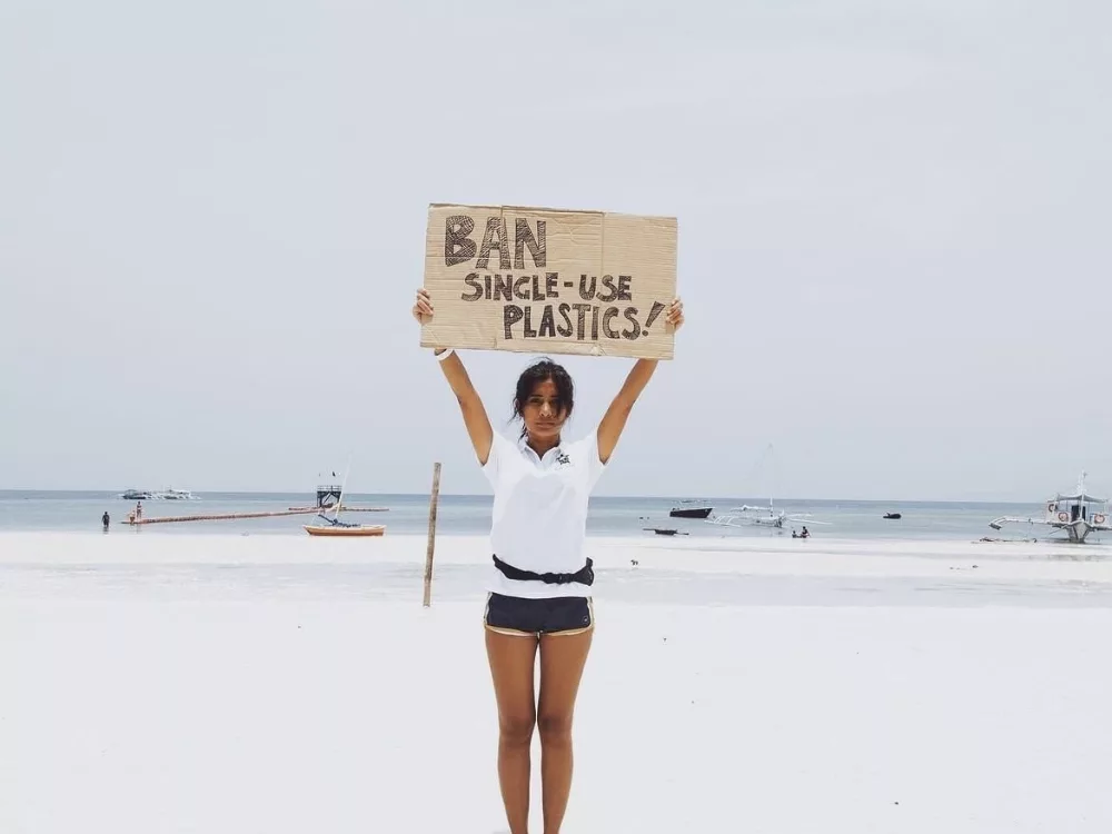 A girl at the ocean holding up a ban single-use plastics sign