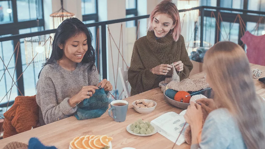 3 young women knitting together at a table